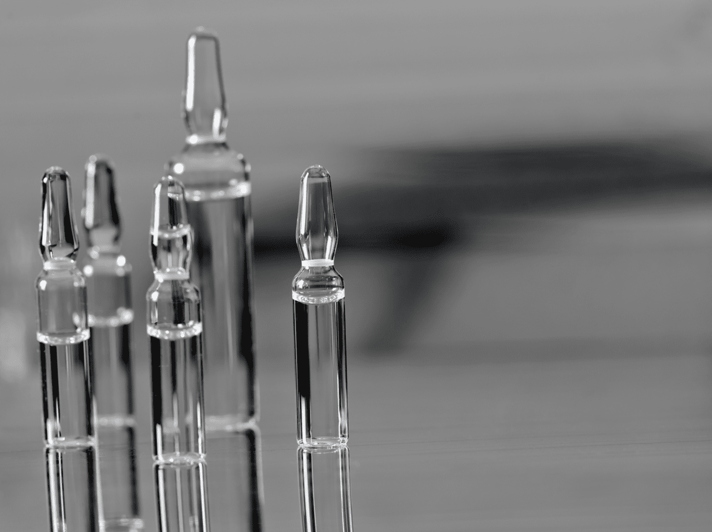 Glass ampoules on reflective gray surface.